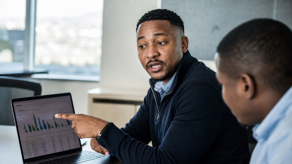 Professional pointing at a data chart on a laptop during the AI for Spreadsheets and Reports workshop